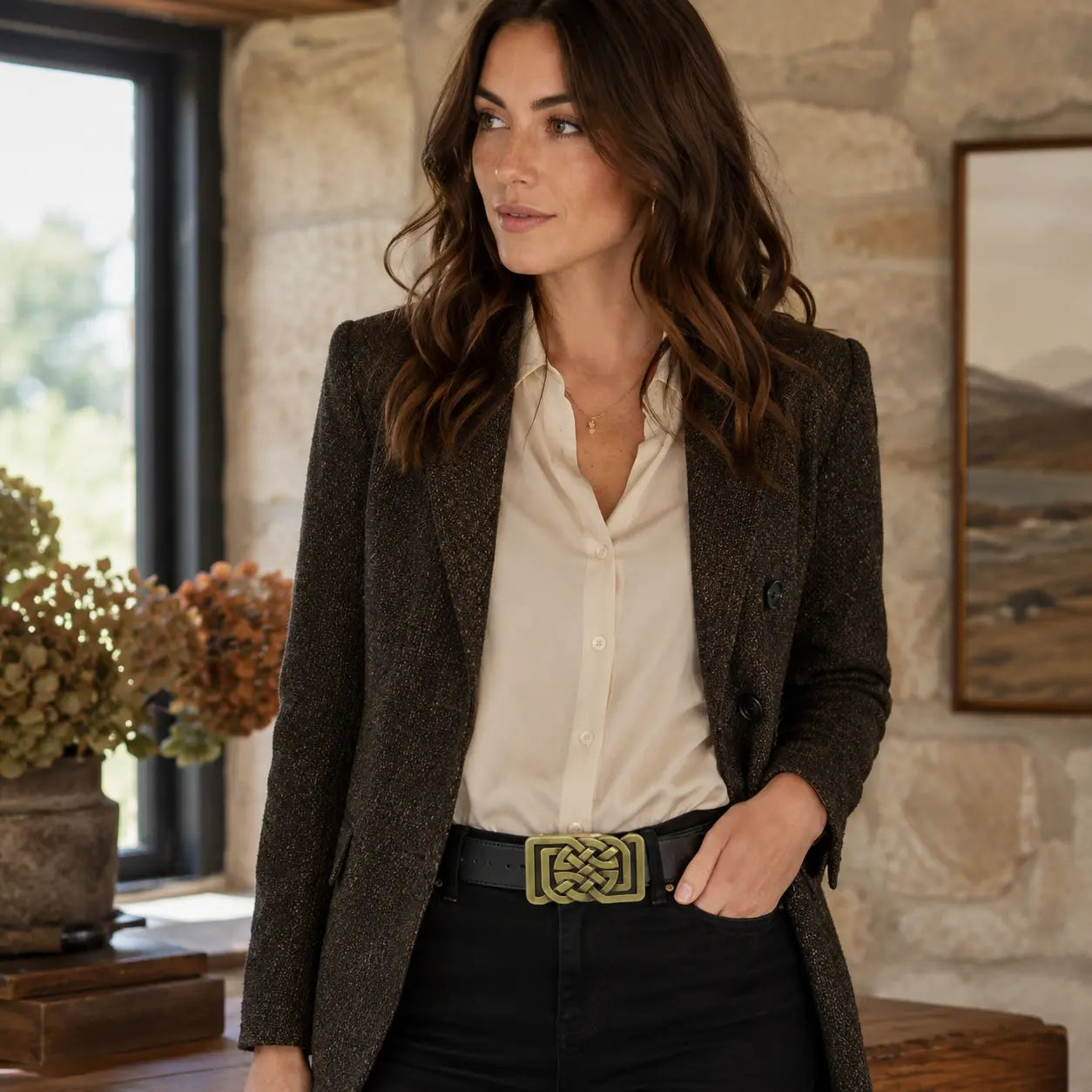 Woman wearing a brown blazer over a white shirt with a celtic bronze belt buckle in a rustic indoor setting.