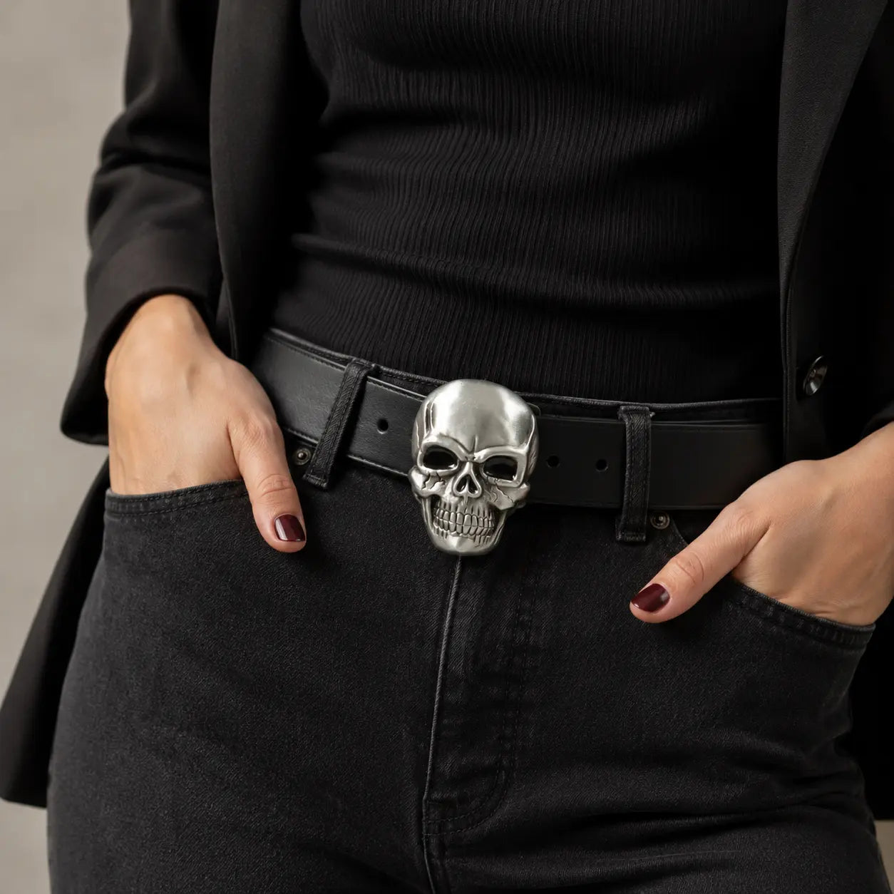 Lady wearing a black outfit with a skull belt buckle on a neutral background