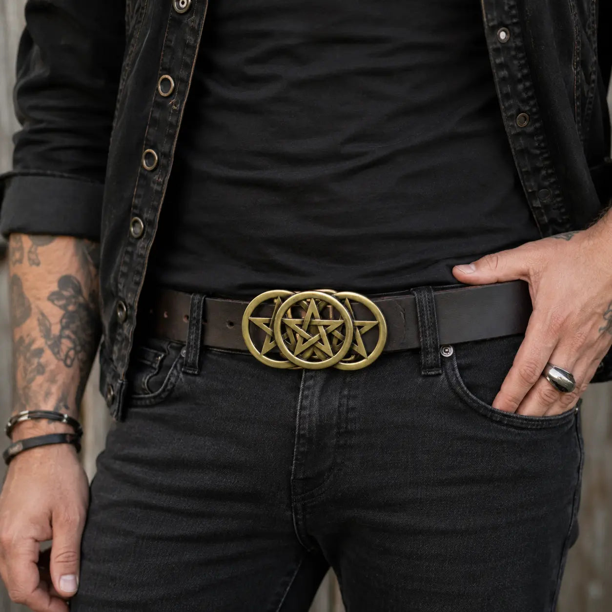 Man wearing a black shirt, black pants, and a belt with a gold pentagram buckle.