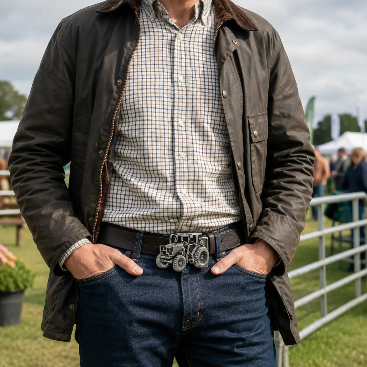Man wearing a dark jacket, checkered shirt, and jeans with a tractor belt buckle outdoors.