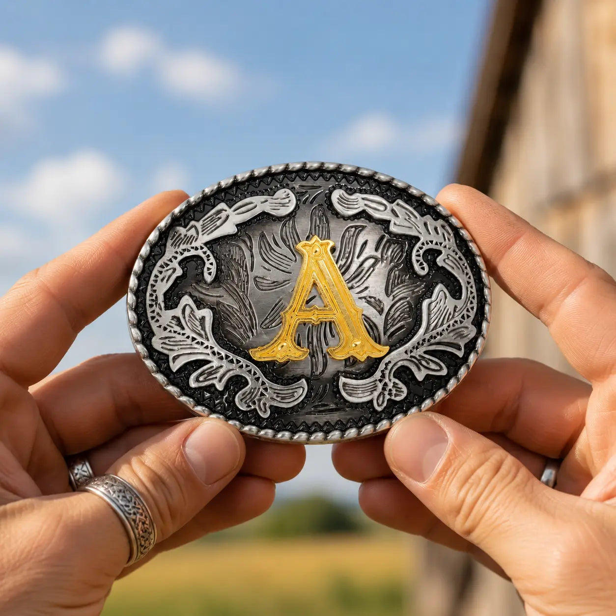 Person holding a decorative belt buckle with a gold 'A' against a blurred natural background