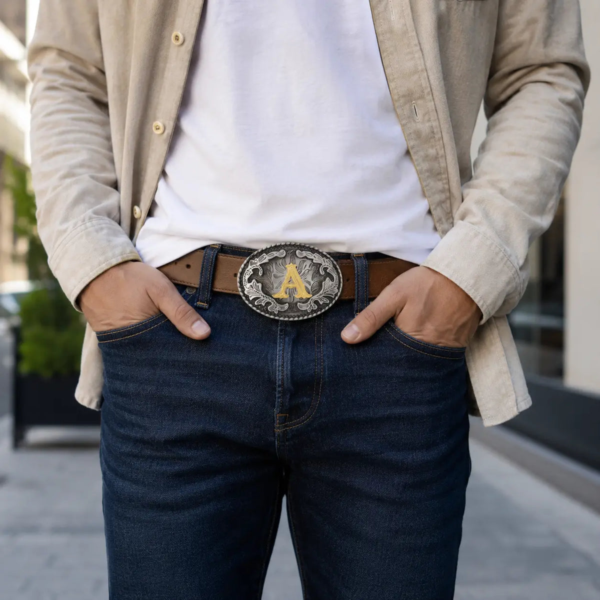 Man wearing a beige jacket, white shirt, dark jeans, and a belt with a decorative buckle.