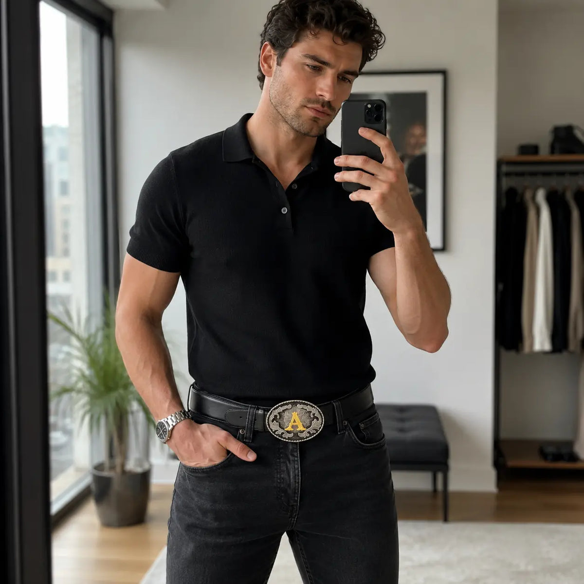 Man taking a mirror selfie wearing a black polo shirt and jeans in a room with letter A belt buckle.