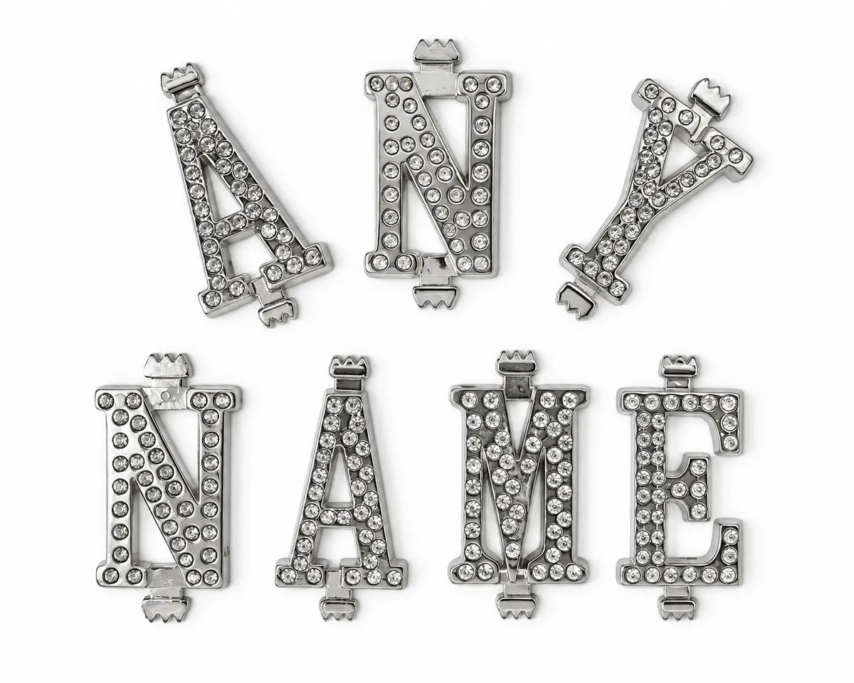 Six silver-tone belt buckle letters embellished with clear rhinestones, arranged on a plain white background.