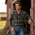 Man wearing a red tractor belt buckle and jeans standing in front of a red barn with a tractor in the background.