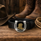 Black belt with a horseshoe and cowboy boot buckle on a wooden surface, surrounded by a cowboy hat, boots, and rope.