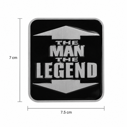 A square black belt buckle with rounded corners, featuring the phrase “THE MAN THE LEGEND” in large metallic silver letters with arrow-like shapes above and below. White dimension lines and text show 7 cm height and 7.5cm