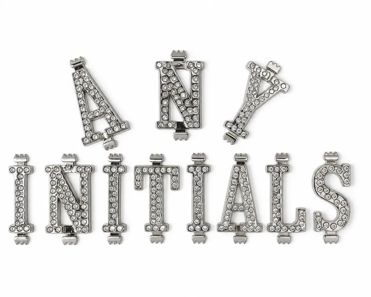 A set of silver-tone belt buckle letters, including A, M, T, S, and Z, embellished with clear rhinestones, arranged on a plain white background.